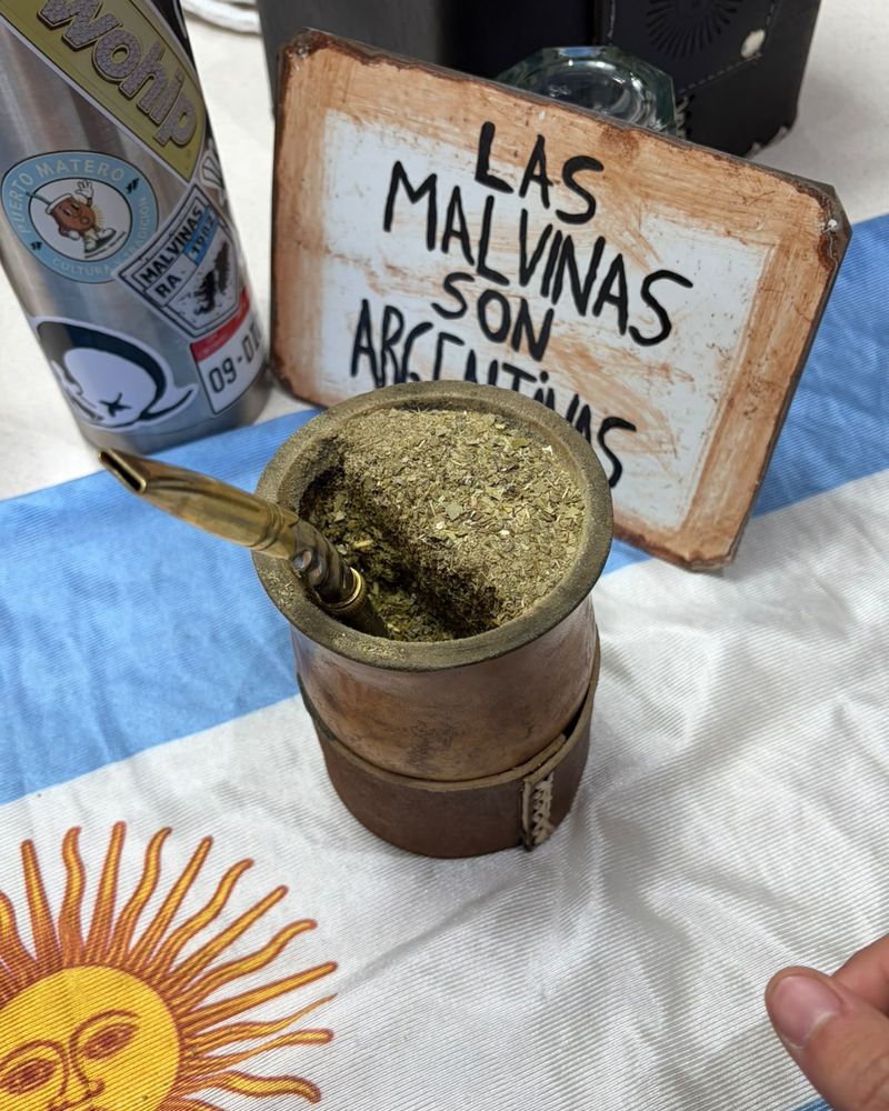 Mate cobrizo con bombilla sobre una bandera argentina, junto a un cartel de Malvinas
