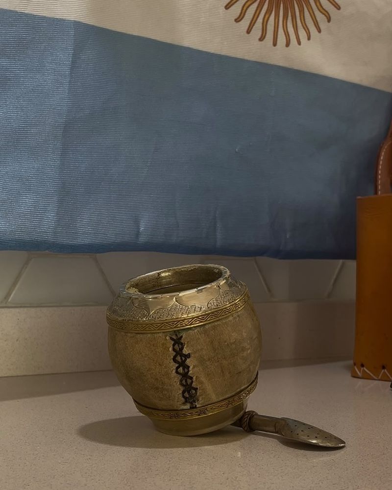 Mate de calabaza con detalles metálicos y bombilla frente a una bandera argentina